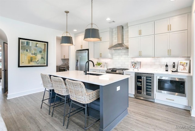 kitchen featuring wall chimney range hood, appliances with stainless steel finishes, a sink, wine cooler, and washer and clothes dryer