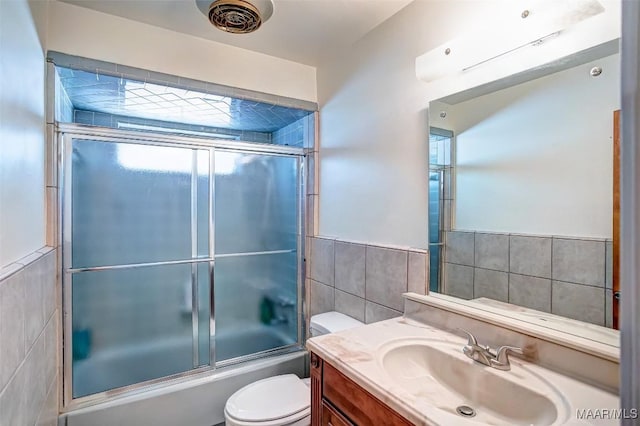 bathroom with toilet, tile walls, bath / shower combo with glass door, and vanity