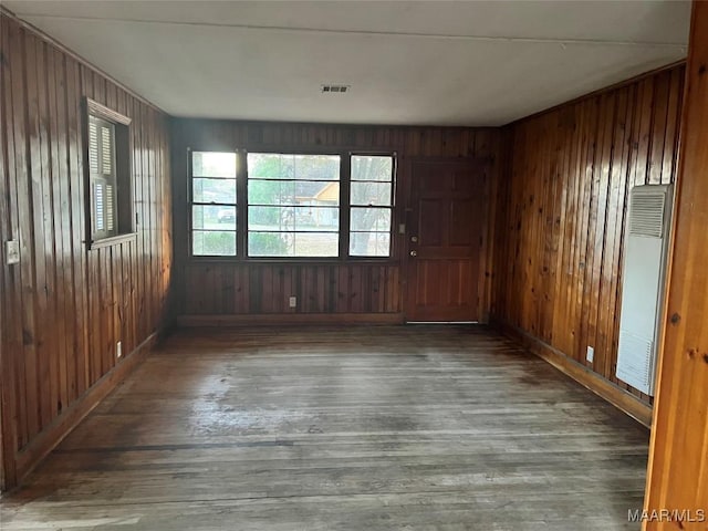 unfurnished room with wooden walls, wood finished floors, and a heating unit