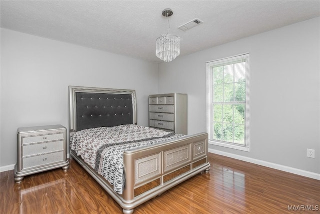 bedroom with visible vents, an inviting chandelier, wood finished floors, baseboards, and a textured ceiling