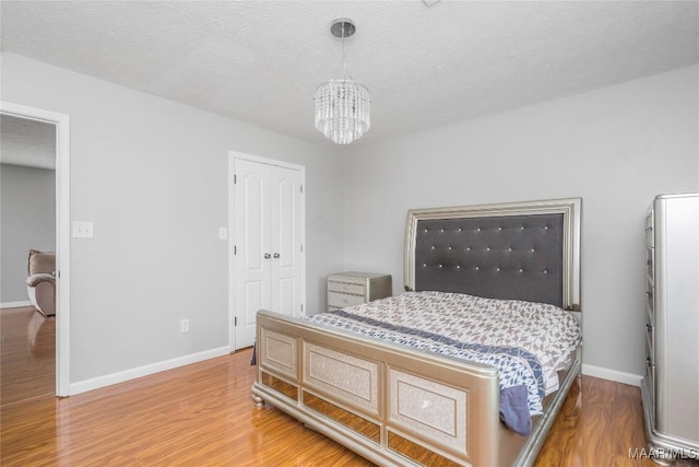 bedroom featuring an inviting chandelier, a textured ceiling, baseboards, and wood finished floors