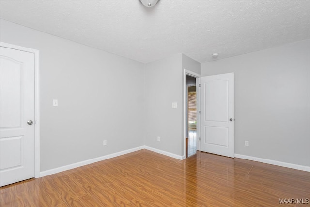 unfurnished room with a textured ceiling, baseboards, and wood finished floors