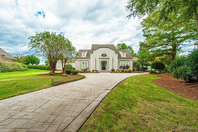 french country inspired facade featuring a front yard, stucco siding, and curved driveway