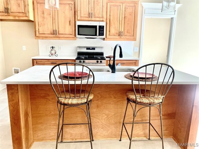 kitchen featuring stainless steel appliances, a breakfast bar, a sink, decorative backsplash, and light countertops