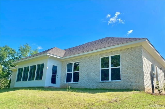 back of property with roof with shingles, brick siding, and a lawn