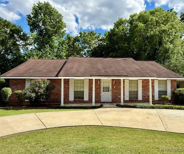 ranch-style home featuring roof with shingles, brick siding, and a front lawn