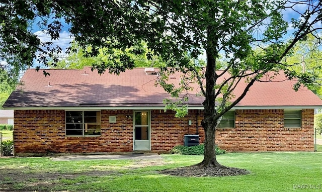 rear view of property featuring a yard, brick siding, a patio area, central air condition unit, and a shingled roof