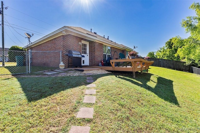back of property featuring a lawn, brick siding, a deck, a fenced backyard, and a gate