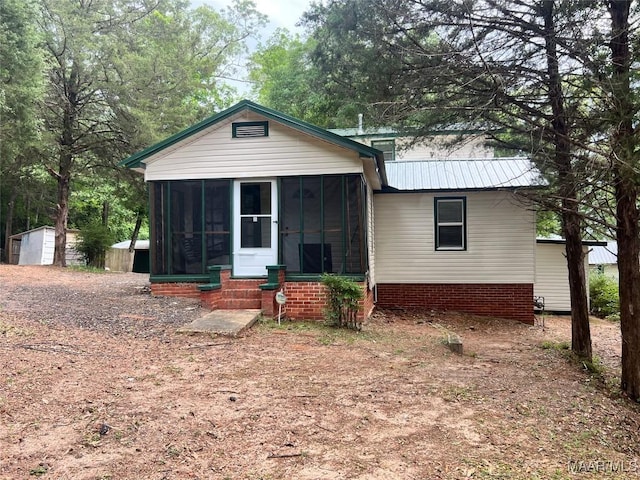 bungalow-style home with a sunroom, a storage shed, an outbuilding, and metal roof