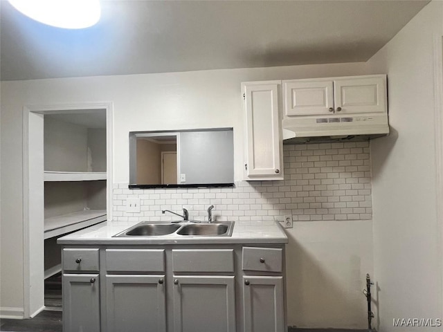 kitchen featuring under cabinet range hood, gray cabinets, tasteful backsplash, and a sink