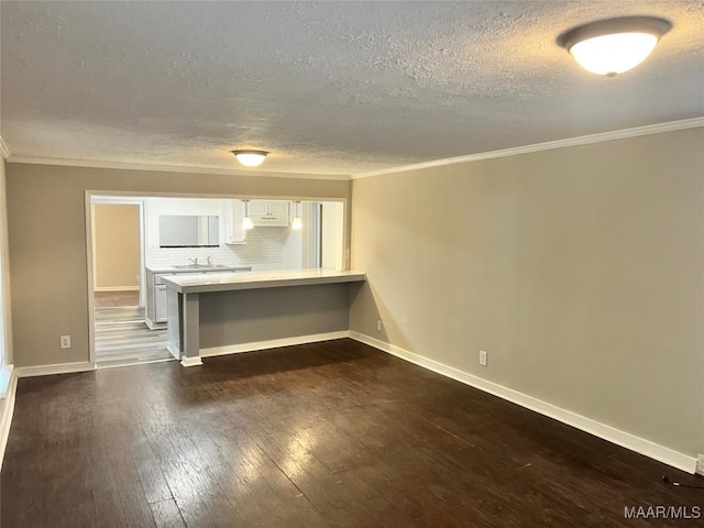 unfurnished living room with crown molding, a textured ceiling, baseboards, and dark wood-style floors