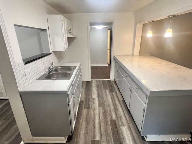 kitchen featuring under cabinet range hood, dark wood finished floors, a sink, a peninsula, and decorative backsplash