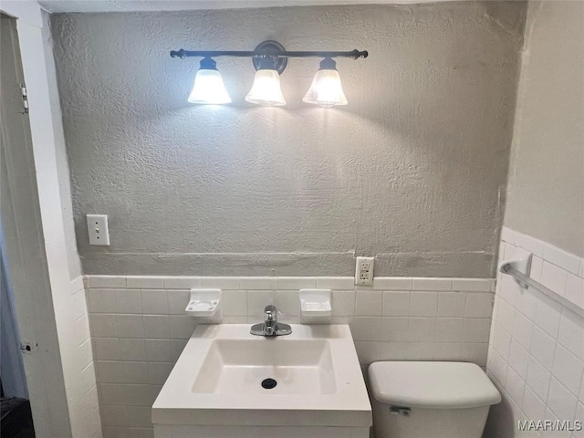 bathroom featuring tile walls, toilet, wainscoting, and vanity