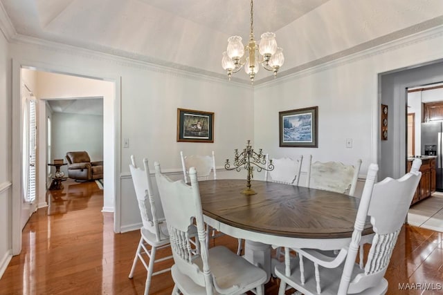 dining space with a raised ceiling, ornamental molding, an inviting chandelier, and wood finished floors