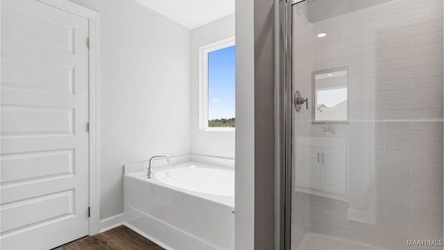 bathroom with baseboards, a shower stall, a bath, and wood finished floors