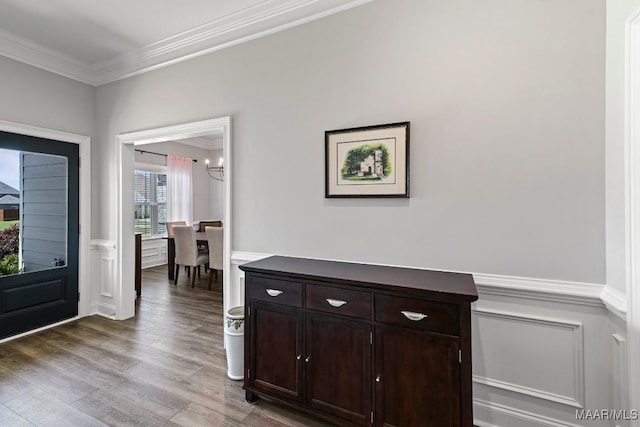 interior space featuring a chandelier, a decorative wall, crown molding, a wainscoted wall, and wood finished floors