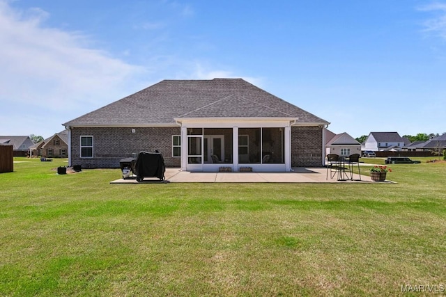 rear view of property featuring a lawn, a patio area, brick siding, and a sunroom