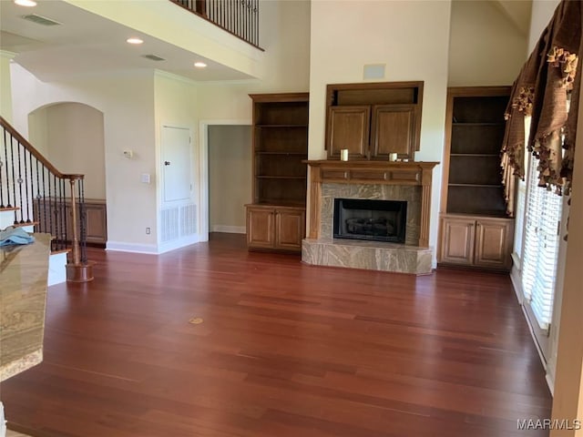 unfurnished living room with stairs, visible vents, dark wood-style flooring, a high ceiling, and baseboards