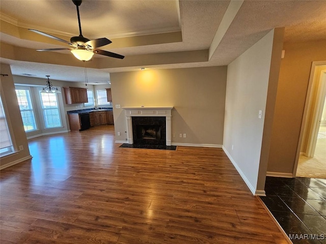 1946 Regent Rd, Prattville, AL 36066 - unfurnished living room featuring ceiling fan with notable chandelier, dark wood-type flooring, a fireplace, a tray ceiling, and baseboards