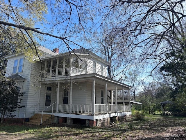 view of side of home featuring a porch, a balcony, and a chimney