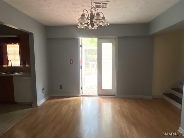 unfurnished dining area featuring light wood-style floors, a chandelier, a textured ceiling, stairway, and a sink