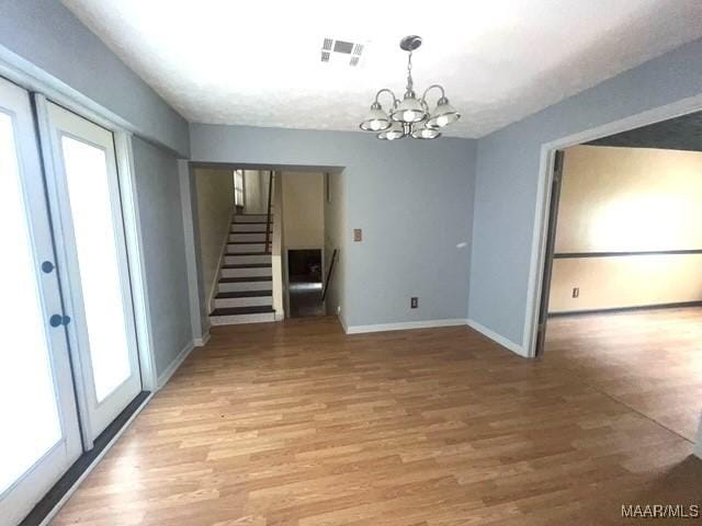 spare room featuring light wood-style flooring, stairs, baseboards, and a chandelier
