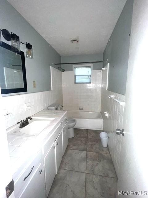 bathroom with tile walls, toilet, vanity, and shower / tub combination