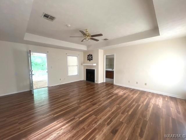 unfurnished living room with a tray ceiling, dark wood finished floors, a ceiling fan, and baseboards