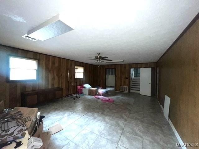 unfurnished living room featuring wooden walls, ceiling fan, and stairs