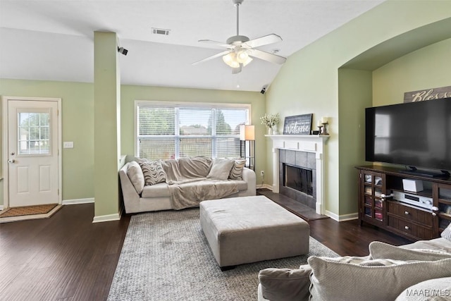 living area with vaulted ceiling, plenty of natural light, wood finished floors, a tiled fireplace, and a ceiling fan