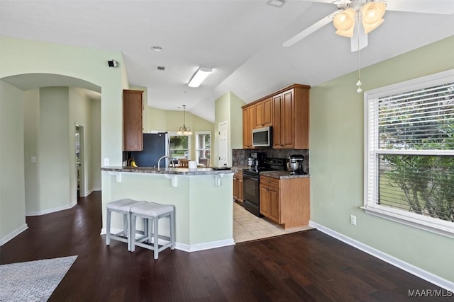 kitchen with stainless steel appliances, arched walkways, a breakfast bar, vaulted ceiling, and light wood-type flooring