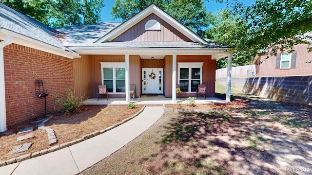 view of front of house with roof with shingles, fence, covered porch, board and batten siding, and brick siding
