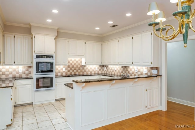 8180 Longneedle Pl, Montgomery, AL 36117 - kitchen featuring stainless steel double oven, a chandelier, white cabinetry, a peninsula, and ornamental molding