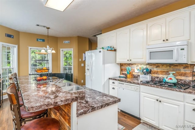 kitchen featuring white appliances, a sink, wood finished floors, tasteful backsplash, and a center island with sink