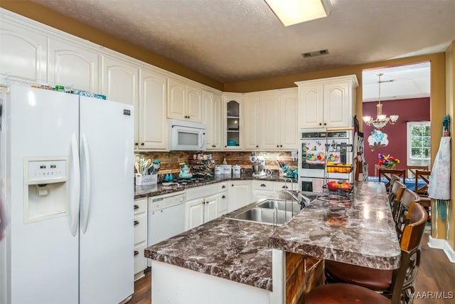 kitchen with white appliances, a sink, dark wood-style flooring, dark countertops, and a chandelier