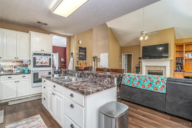 kitchen with a sink, double oven, open floor plan, ceiling fan, and a tiled fireplace