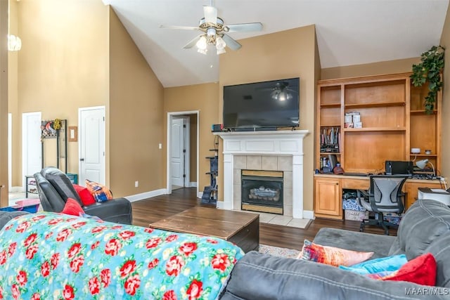 living room with a ceiling fan, an office area, dark wood-style flooring, a tiled fireplace, and high vaulted ceiling