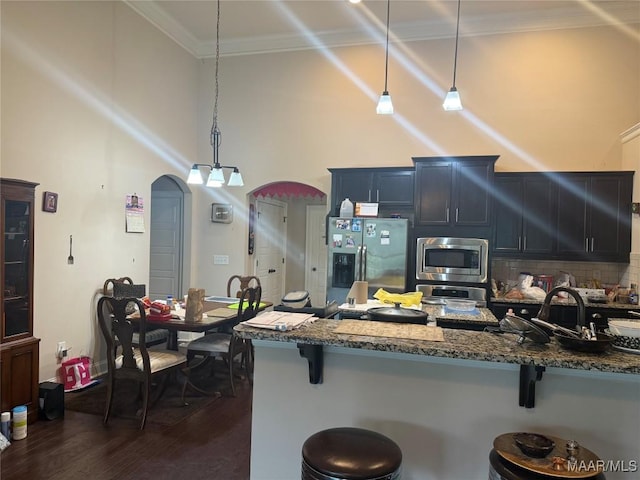 kitchen featuring appliances with stainless steel finishes, a breakfast bar, dark wood finished floors, dark stone countertops, and a towering ceiling