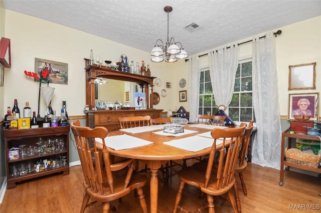 dining area with wood finished floors, a chandelier, and a textured ceiling