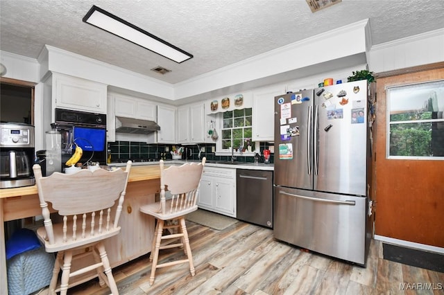 kitchen with stainless steel appliances, crown molding, a textured ceiling, light wood-style floors, and white cabinets