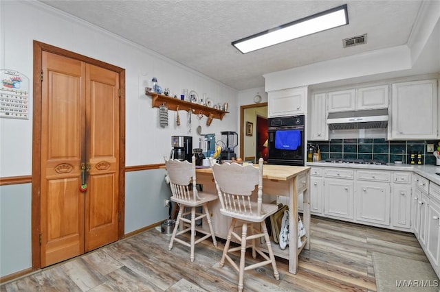 kitchen featuring under cabinet range hood, light wood-style floors, white cabinets, light countertops, and decorative backsplash