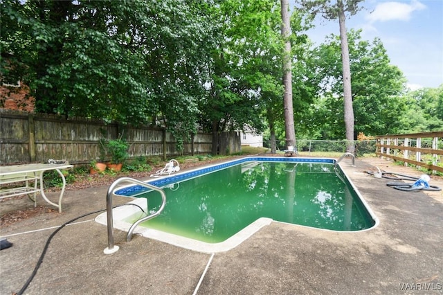 view of swimming pool with a fenced backyard, a patio, and view of scattered trees
