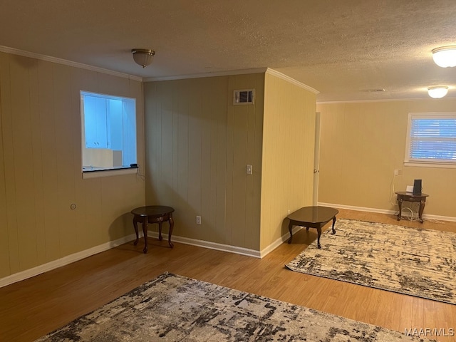 spare room featuring wood finished floors, ornamental molding, baseboards, a textured ceiling, and wooden walls