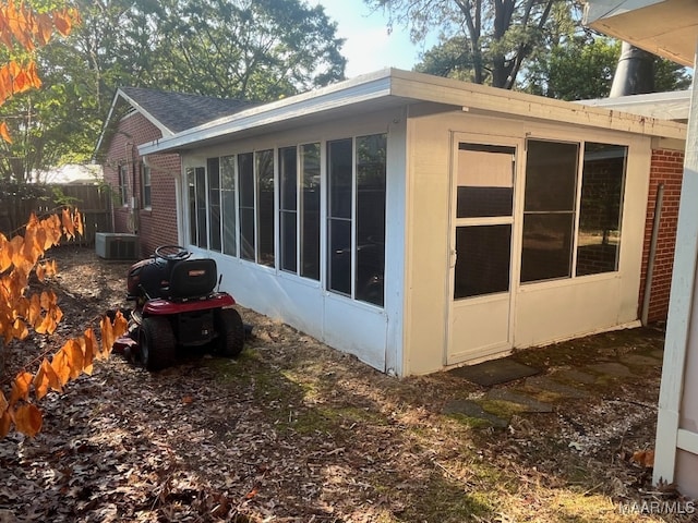 view of side of home with a sunroom, brick siding, central AC, and fence