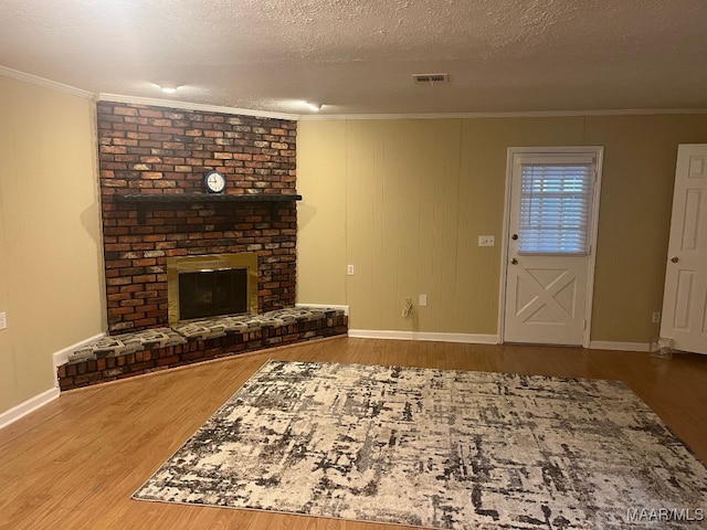 unfurnished living room with wood finished floors, ornamental molding, a fireplace, baseboards, and a textured ceiling