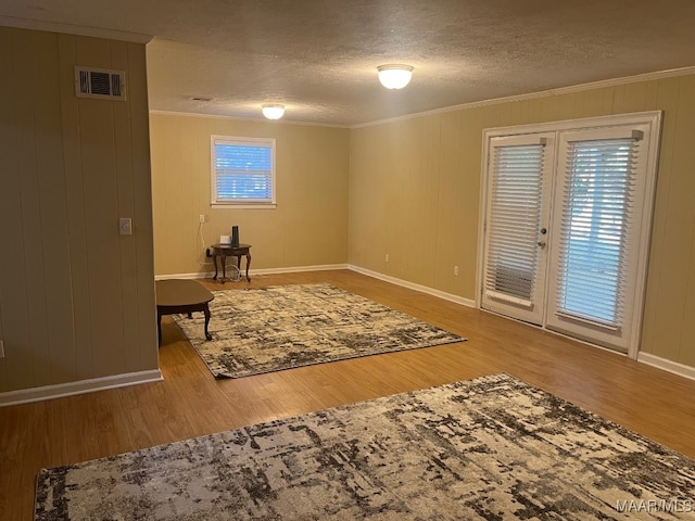 living area featuring ornamental molding, wood finished floors, baseboards, a textured ceiling, and french doors