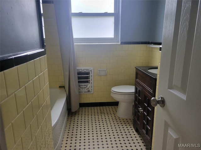 full bath with tile walls, heating unit, toilet, wainscoting, and vanity