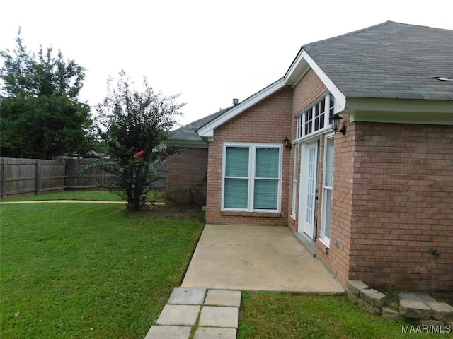 view of property exterior with brick siding, a patio area, and roof with shingles