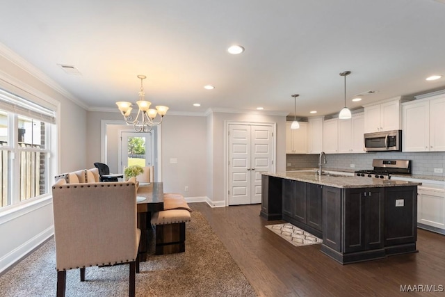 kitchen with stainless steel appliances, an island with sink, white cabinetry, a chandelier, and baseboards