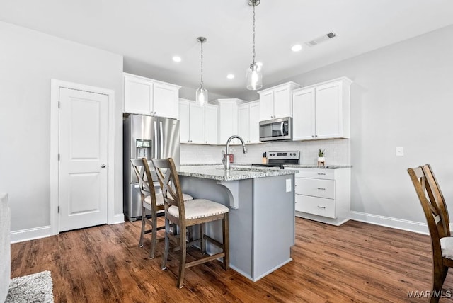 kitchen featuring stainless steel appliances, a breakfast bar, decorative backsplash, white cabinetry, and a kitchen island with sink